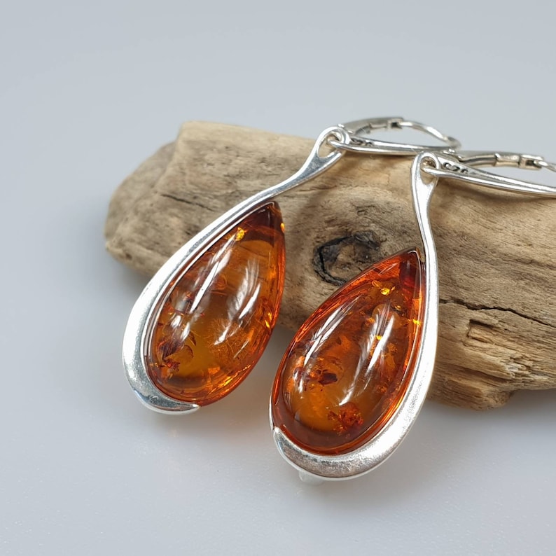 May include: A pair of silver teardrop earrings with amber stones. The earrings have a smooth, curved design and are suspended from silver hooks.