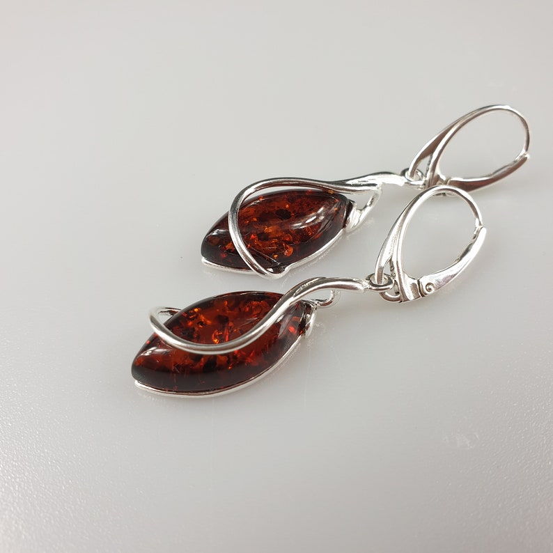May include: A pair of silver earrings with amber teardrop-shaped stones. The earrings have a simple, elegant design.