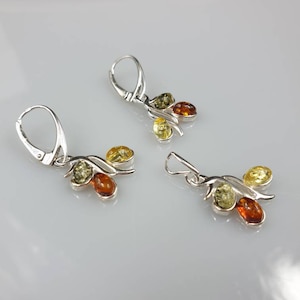 Op de afbeelding: Een paar zilveren oorbellen met elk drie amberstenen. De stenen zijn groen, geel en oranje.
