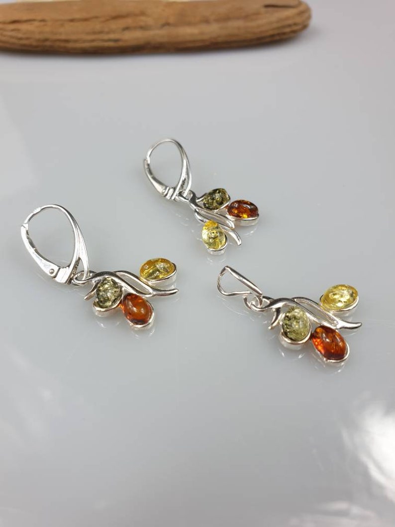 Op de afbeelding: Een paar zilveren oorbellen met elk drie amberstenen. De stenen zijn groen, geel en oranje.