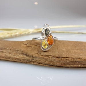 May include: A silver ring featuring three amber stones in a swirling design. The stones are yellow, orange, and green.