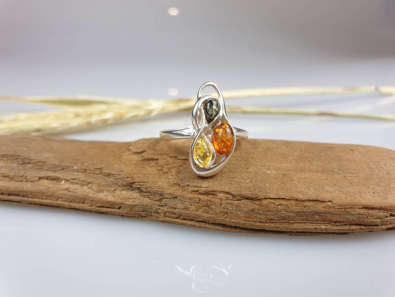 May include: A silver ring featuring three amber stones in a swirling design. The stones are yellow, orange, and green.