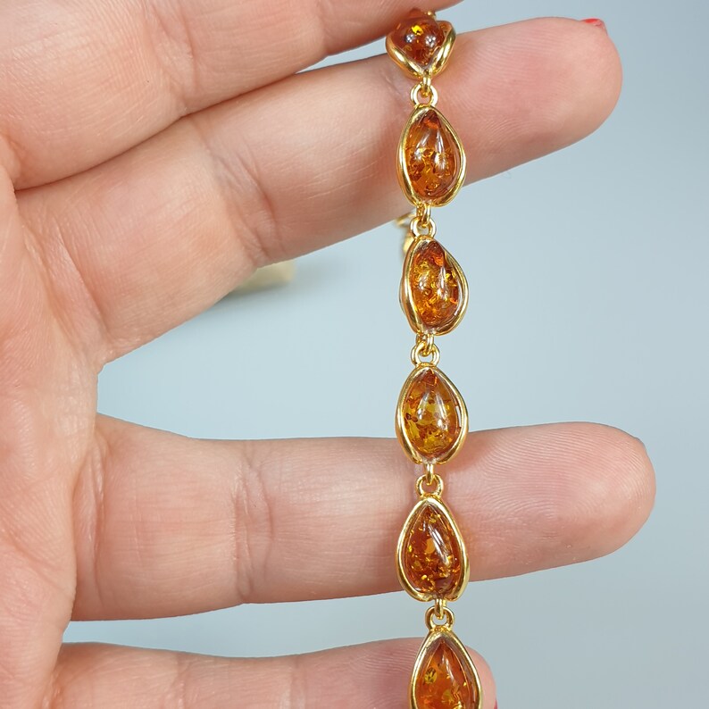 May include: A gold chain bracelet with amber teardrop-shaped beads. The bracelet is on a hand.