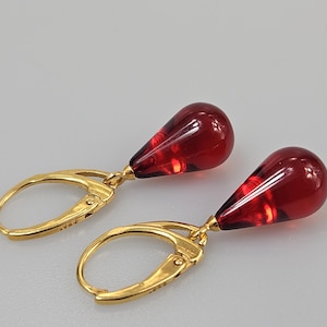 Peut inclure: Une paire de boucles d'oreilles pendantes avec des pendentifs rouges translucides en forme de goutte d'eau. Les boucles d'oreilles ont des fermoirs à levier dorés. Les pendentifs rouges ont un motif interne texturé.
