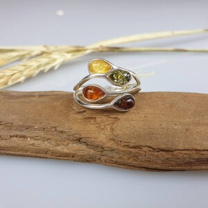 May include: A silver ring featuring three teardrop-shaped amber stones in shades of yellow, orange, and green.