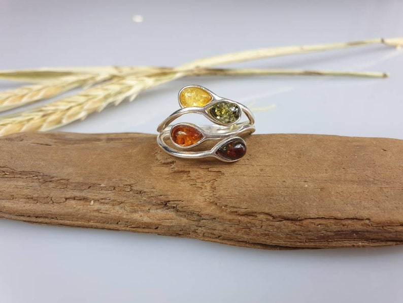 May include: A silver ring featuring three teardrop-shaped amber stones in shades of yellow, orange, and green.
