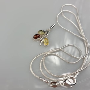 Op de afbeelding: Een zilveren ketting met een hanger met drie amberstenen in tinten geel, oranje en bruin.