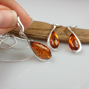 May include: A silver necklace and earrings set with amber teardrop pendants. The necklace has a silver chain and the earrings are dangle style.