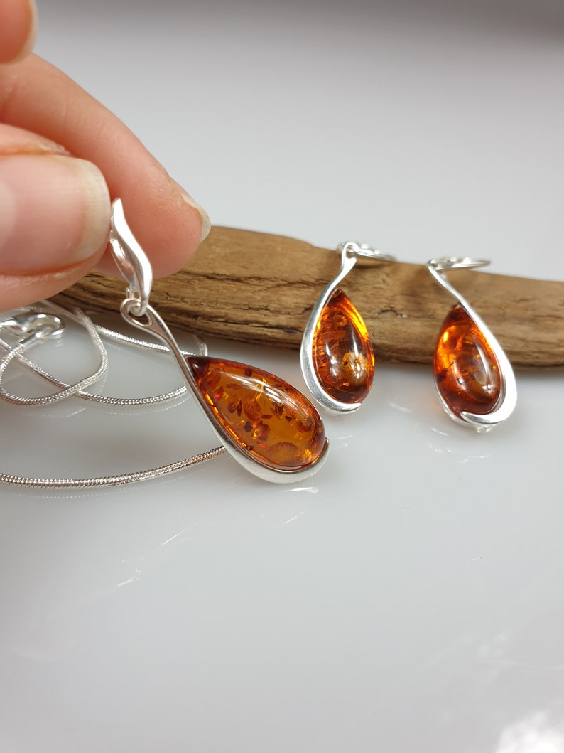 May include: A silver necklace and earrings set with amber teardrop pendants. The necklace has a silver chain and the earrings are dangle style.