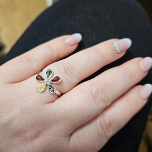 May include: A silver ring with a flower design featuring five amber stones in shades of yellow, orange, and green.