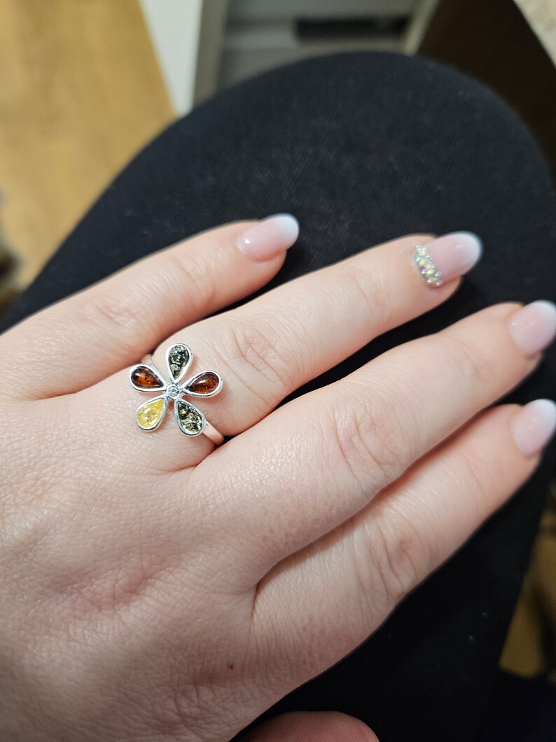 May include: A silver ring with a flower design featuring five amber stones in shades of yellow, orange, and green.