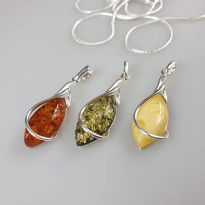 May include: Three silver pendants with amber stones. The stones are different colors: orange, green, and yellow.