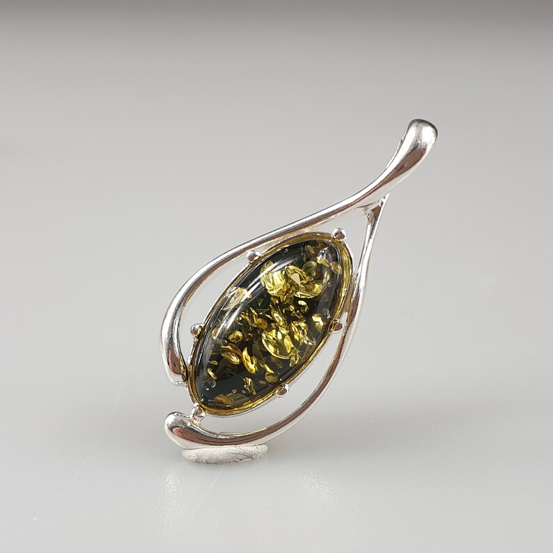 May include: A silver pendant with a green amber stone in an oval shape. The pendant is shaped like a leaf with a delicate design.
