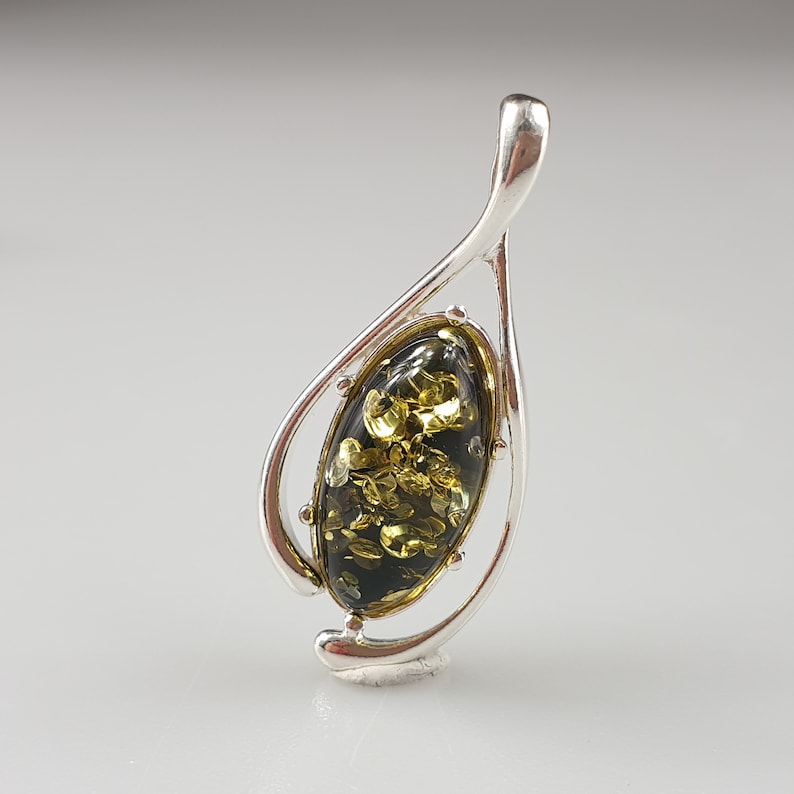 May include: A silver pendant with a green and gold amber stone in an oval shape. The pendant is designed in a leaf shape with a bail at the top.