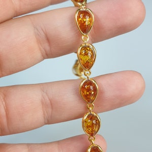 May include: A gold chain bracelet with oval-shaped amber stones. The stones are a rich, honey color and are set in a polished gold frame.
