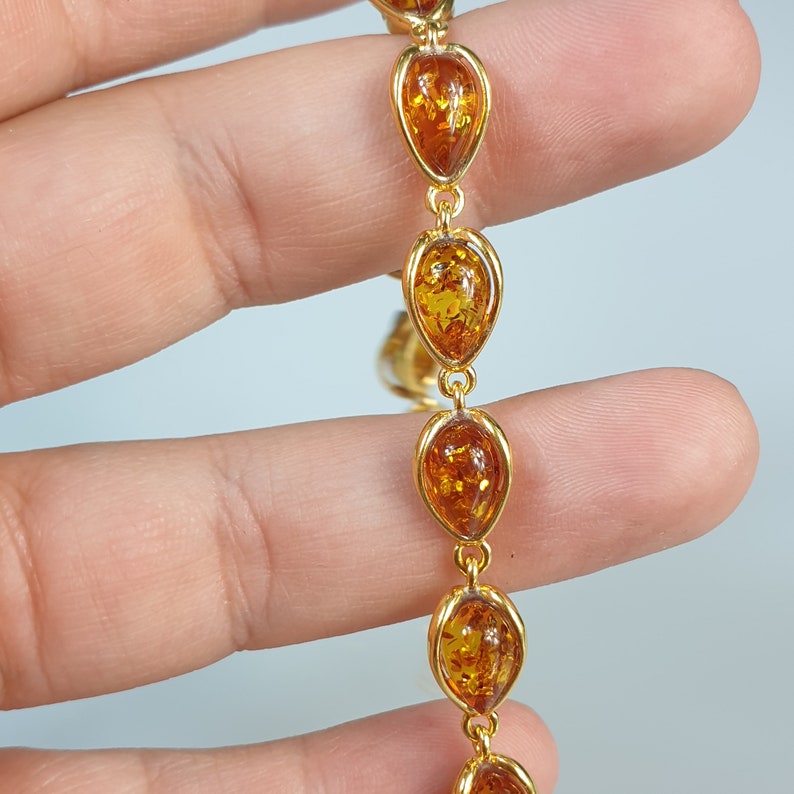 May include: A gold chain bracelet with oval-shaped amber stones. The stones are a rich, honey color and are set in a polished gold frame.