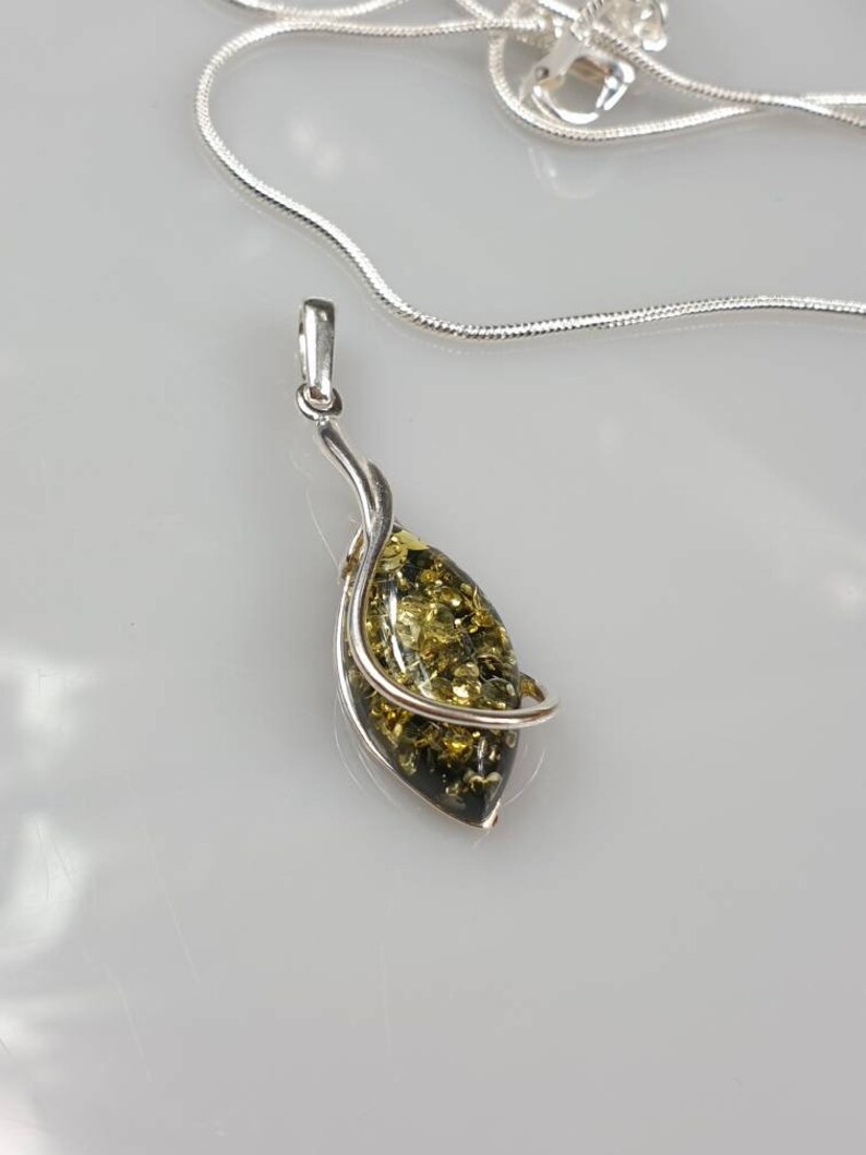 May include: A silver chain necklace with a pendant featuring a green and gold amber stone wrapped in silver.