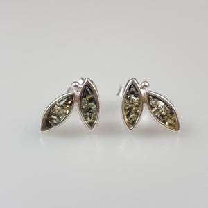 May include: A pair of silver stud earrings with a leaf design. Each earring has two leaf-shaped sections filled with a speckled, light green material. The earrings have a polished, reflective finish, set against a soft, neutral background.