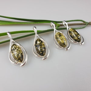 May include: Four silver pendants with green amber stones. Each pendant features a teardrop-shaped design with a delicate silver frame.