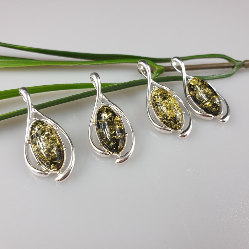 May include: Four silver pendants with green amber stones. Each pendant features a teardrop-shaped design with a delicate silver frame.