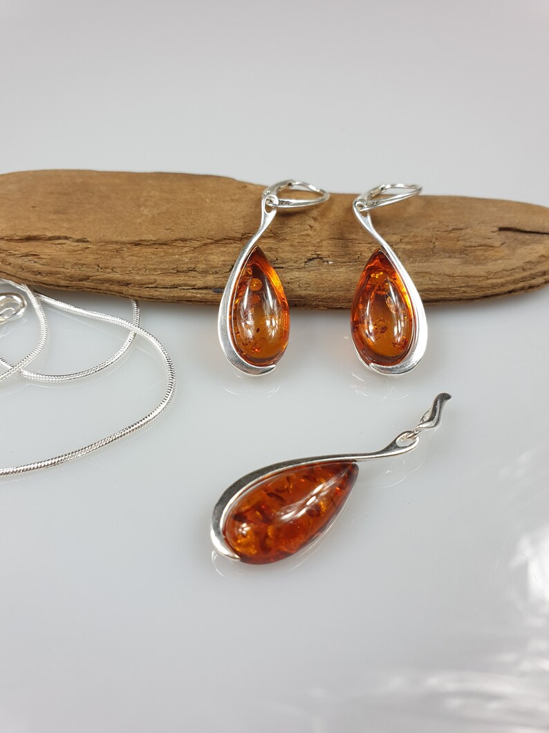 May include: A set of amber earrings and a pendant necklace with silver settings. The amber is a warm, honey color and the silver is polished.