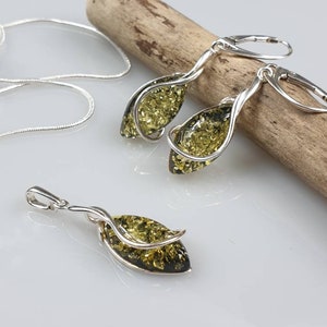 May include: A set of amber earrings and a pendant necklace with silver twisted wire accents. The amber stones are a dark green color.