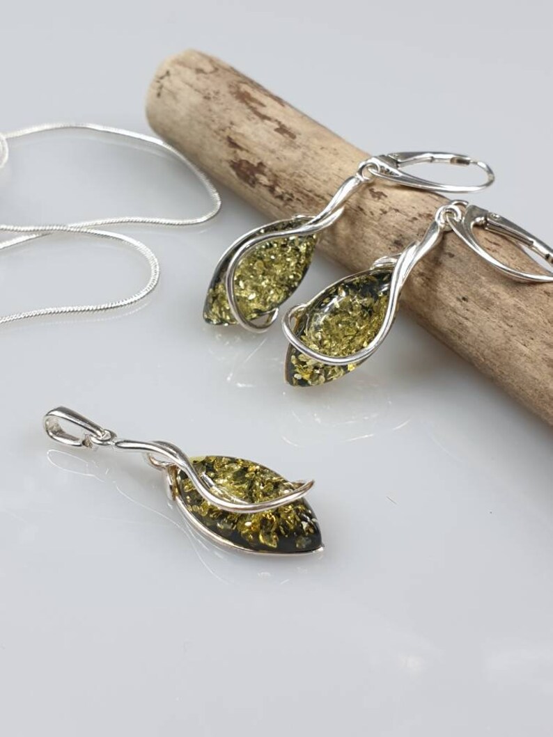 May include: A set of amber earrings and a pendant necklace with silver twisted wire accents. The amber stones are a dark green color.