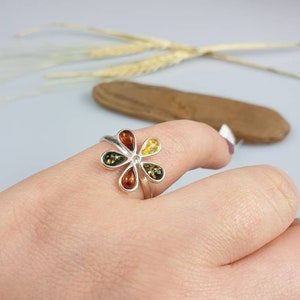 May include: A silver ring with a flower design featuring five amber stones in shades of yellow, orange, and brown.