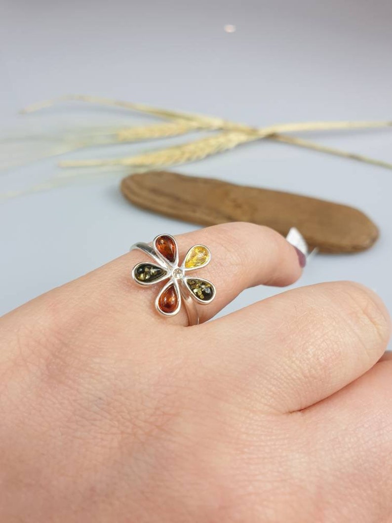 May include: A silver ring with a flower design featuring five amber stones in shades of yellow, orange, and brown.
