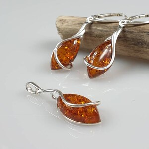 May include: A set of amber earrings and a pendant with silver wire wrapped around the amber stones. The earrings are dangle style and the pendant has a bail for a chain.