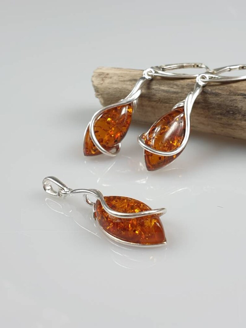 May include: A set of amber earrings and a pendant with silver wire wrapped around the amber stones. The earrings are dangle style and the pendant has a bail for a chain.