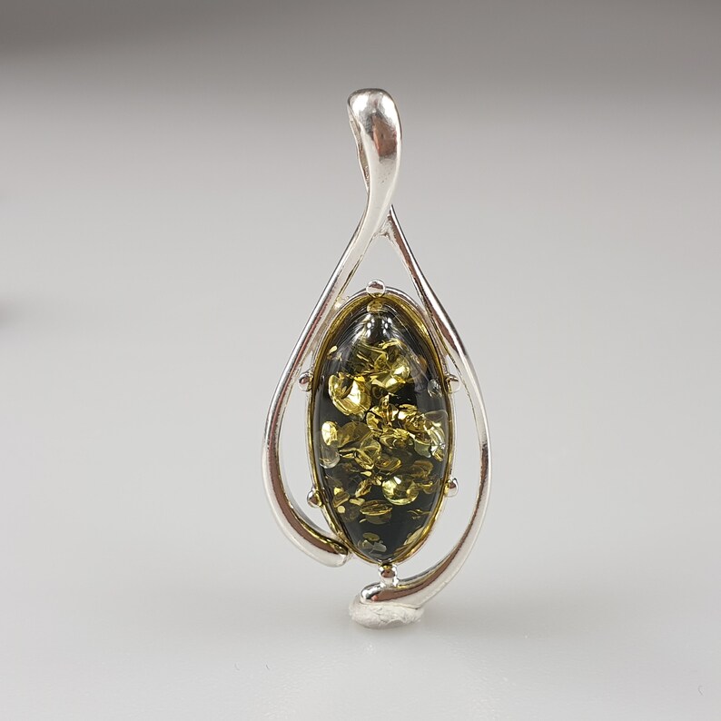 May include: A silver pendant with a green and gold amber stone in an oval shape. The pendant is in the shape of a teardrop.