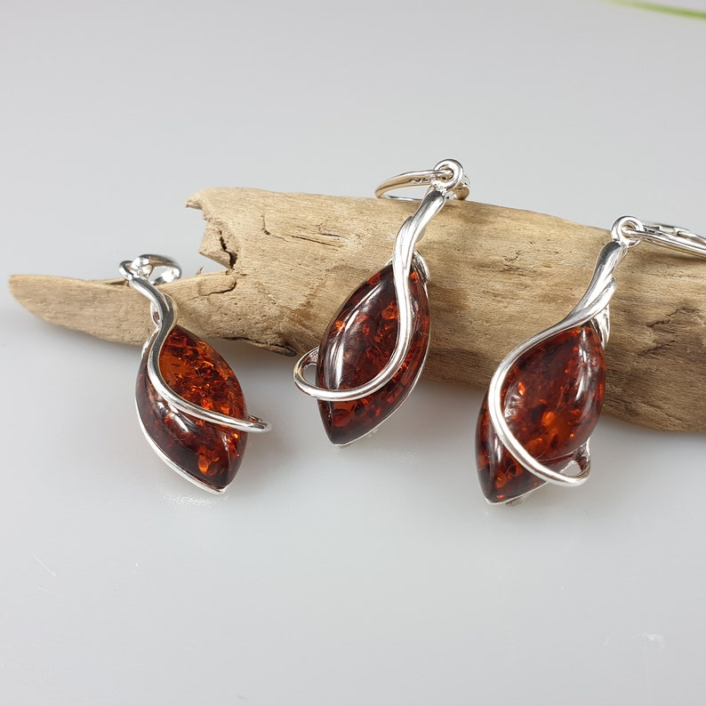 May include: A set of three amber and silver pendant necklaces. Each pendant features a teardrop-shaped amber stone set in a silver swirl design.