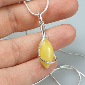 May include: A silver chain necklace with a yellow gemstone pendant. The pendant is wrapped in a silver wire design.
