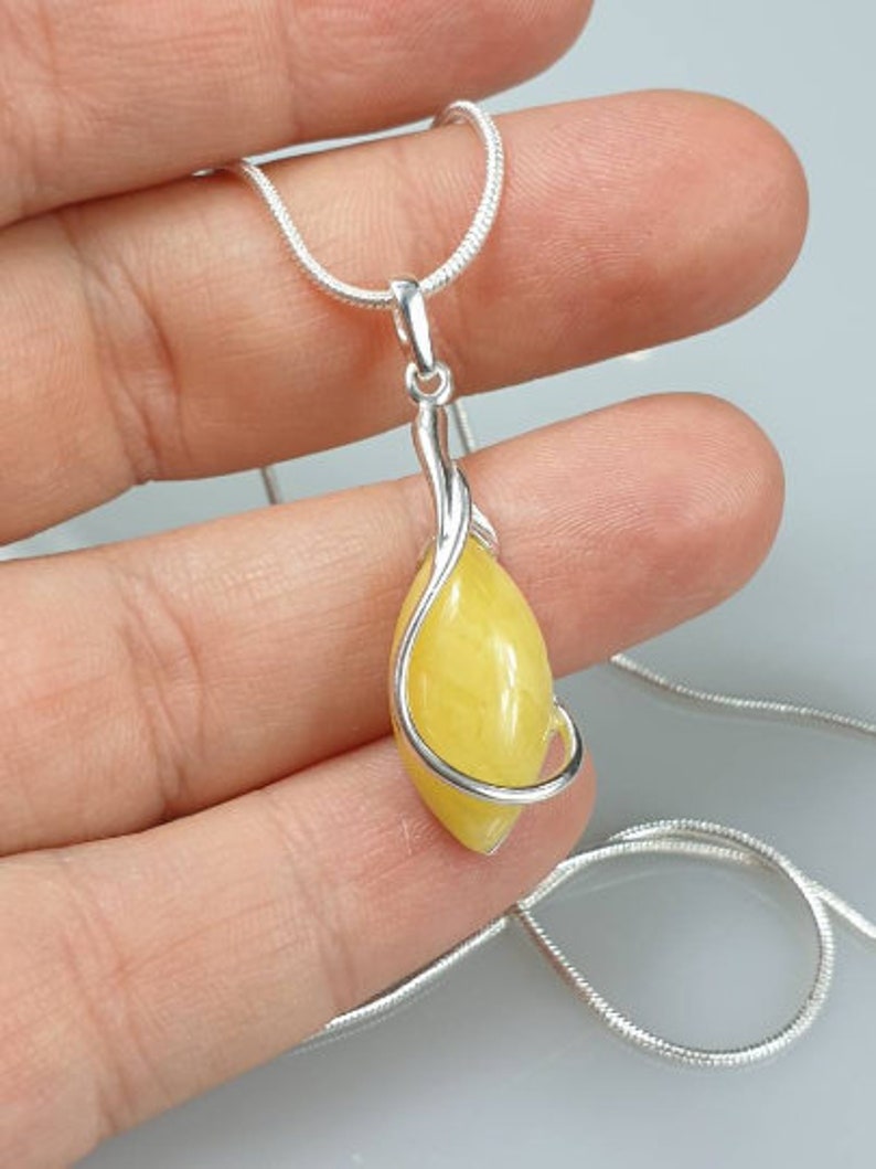 May include: A silver chain necklace with a yellow gemstone pendant. The pendant is wrapped in a silver wire design.