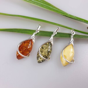 May include: Three amber pendants in silver settings. The pendants are shaped like teardrops and are set in a twisted silver wire design. The amber is a variety of colors, including orange, green, and yellow.