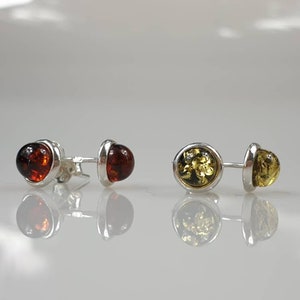 May include: A pair of silver stud earrings with amber stones. One earring has a dark amber stone, and the other has a light amber stone.
