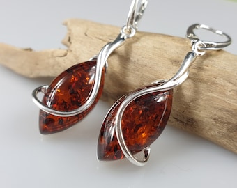 May include: A pair of silver earrings with amber stones. The amber stones are a marbled brown color and are set in a silver wire that is twisted into a leaf shape.