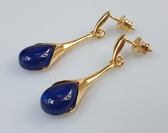May include: A pair of gold earrings with blue teardrop-shaped stones. The earrings have a simple design with a small gold loop at the top and a larger gold loop at the bottom that holds the stone.