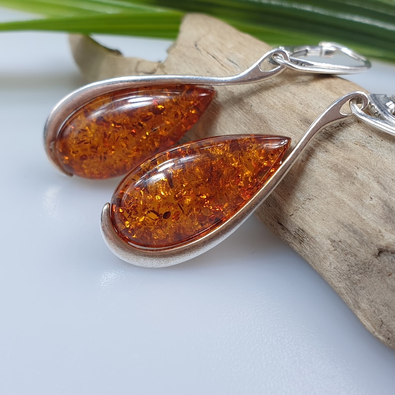 May include: A pair of silver teardrop earrings with amber stones. The earrings have a simple design and are perfect for everyday wear.