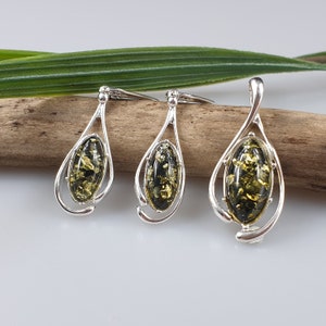 May include: A set of three silver pendant necklaces with green amber stones. The pendants are oval shaped and have a delicate, swirling design.