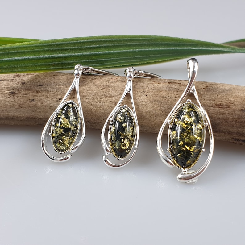 May include: A set of three silver pendant necklaces with green amber stones. The pendants are oval shaped and have a delicate, swirling design.