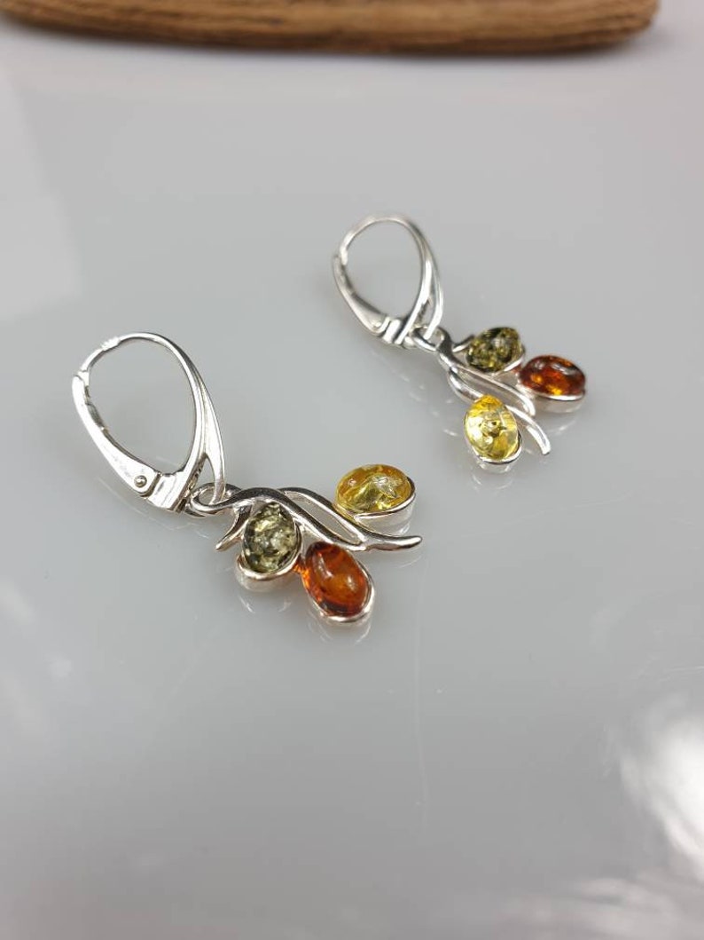 Op de afbeelding: Zilveren oorhangers met drie amberstenen in tinten geel, groen en oranje.