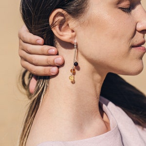 May include: A pair of silver dangle earrings with amber beads in shades of yellow, orange, and brown.