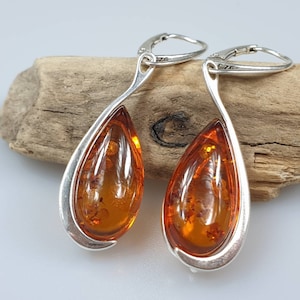 May include: A pair of silver teardrop earrings with amber stones. The earrings have a curved design and are set with a single amber stone in each earring.