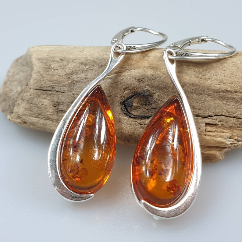 May include: A pair of silver teardrop earrings with amber stones. The earrings have a curved design and are set with a single amber stone in each earring.