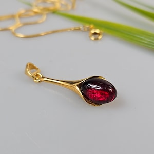 Może przedstawiać: Złoty naszyjnik z czerwonym kamieniem szlachetnym. Zawieszka ma kształt łzy i gładkie, polerowane wykończenie.
