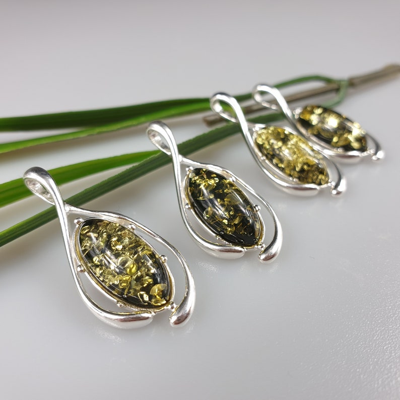 May include: Four silver pendants with green amber stones. Each pendant is shaped like a teardrop and has a twisted design.