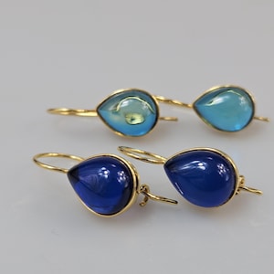 Puede incluir: Un par de pendientes de gota de oro con piedras de vidrio azul y azul claro.