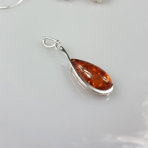 May include: A silver pendant with a teardrop-shaped amber stone.
